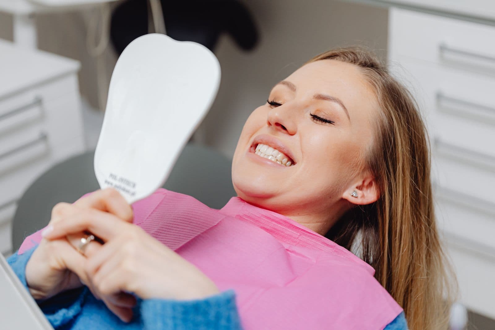 Patient smiling at her new teeth in a hand mirror